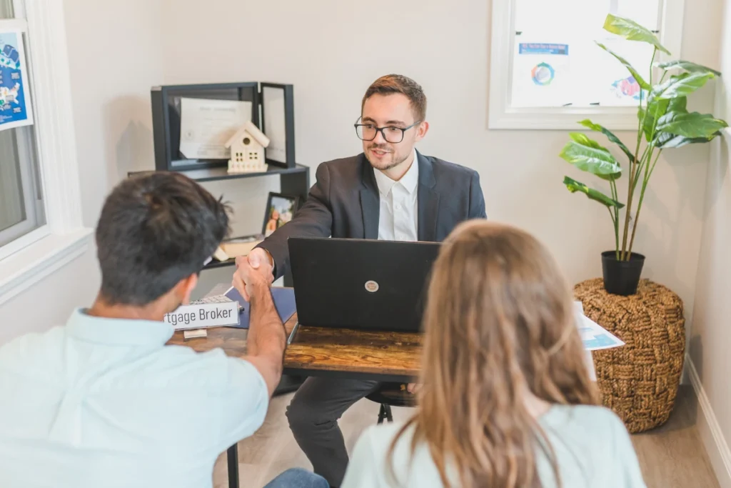 Man in suit shaking hands with mortgage broker from trusted mortgage providers UAE, representing mortgage lenders in Dubai, with woman and documents in office setting